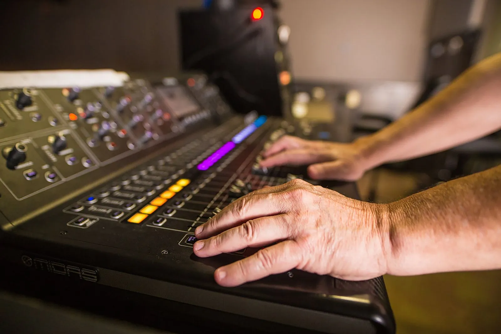 Close-up of hands operating a professional audio mixer console in a studio setting.